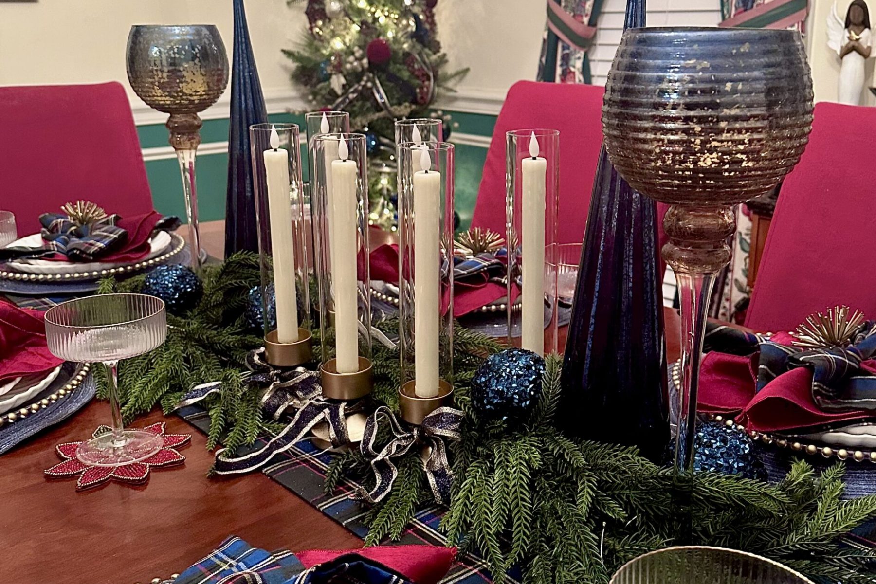 Christmas dining table and tree décor. Deep blue and gold Christmas dining table decorated with flameless candles, garland, and plaid table runner